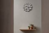 A modern silver bubble cluster wall sconce mounted on a warm gray wall above a wooden floating shelf with two small potted succulents.