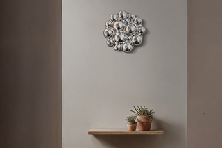 A modern silver bubble cluster wall sconce mounted on a warm gray wall above a wooden floating shelf with two small potted succulents.