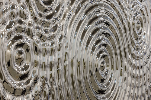 Close-up view of a silver glass panel showcasing detailed ripples and reflections, perfect for modern decor applications.
