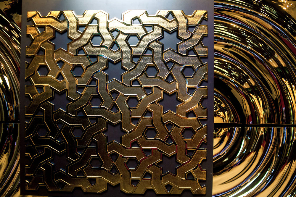 A decorative glass wall panel featuring an intricate golden Eastern geometric pattern with interlocking stars and hexagons on a dark background