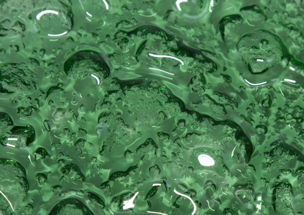 Close-up of Flora green glass wall panel in vibrant green with an organic, liquid-like texture and a reflective surface