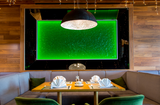 Green backlit Flora wall panel appears in a high-end dining area, framed by wooden elements and sophisticated interior decor