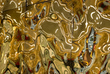 Luxury wall panels – Close-up of the luxury glass wall panel "Aqua High Wave" in a gold finish, with light reflecting off the panels
