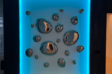 Modern wall art featuring 3D metallic drops on an illuminated panel with blue backlighting