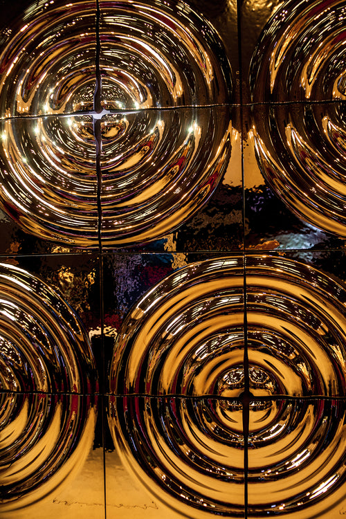Close-up of reflective golden glass wall panels 'X4' with circular patterns with a dynamic light and depth effect.