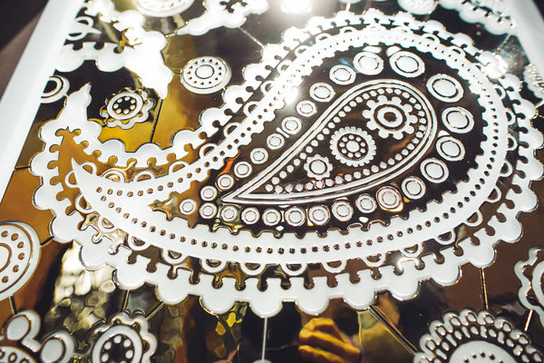 Close-up of the Paisley Pattern – mirrored glass wall panel featuring intricate floral and paisley designs in gold and silver tones.
