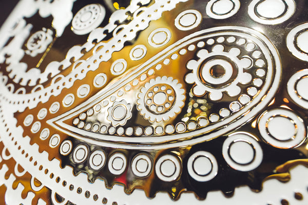 Angled close-up shot of the Paisley Pattern mirrored glass wall panel focusing on the ornamental paisley details with a shimmering metallic finish.