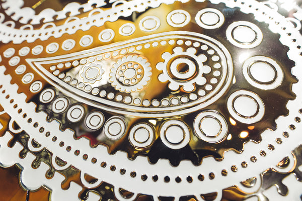 A close-up shot of the Paisley Pattern mirrored glass wall panel focusing on the ornamental paisley details with a shimmering metallic finish.