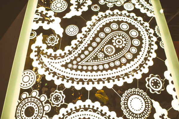 The Paisley Pattern mirrored glass wall panel illuminated, showcasing its intricate paisley and floral designs with reflective and frosted details.