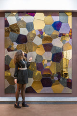 A woman standing in front of a large polygonal mosaic wall panel at an exhibition. The glass textures and metallic hues create a captivating display.