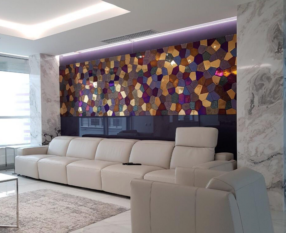 A close-up of a polygonal glass mosaic wall panel with iridescent, gold, and bronze tones. The textured glass reflects light dynamically.