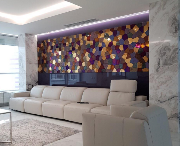 A polygonal mosaic wall panel installed in a luxury living room. The vibrant glass tiles create a stunning accent above a modern white sofa.