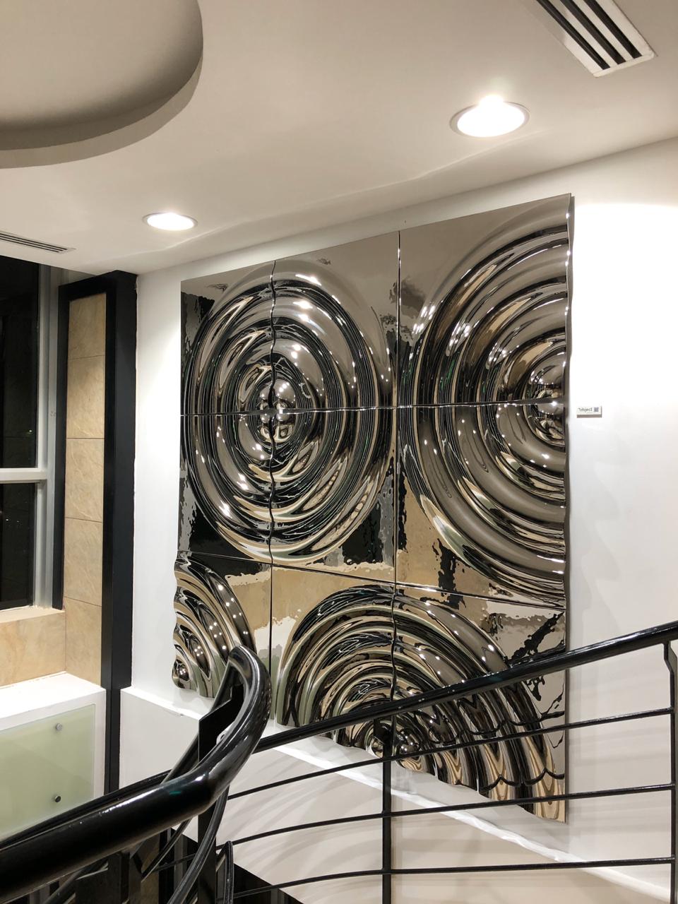 Reflective modular silver glass wall panels  with circular patterns in a modern interior near a staircase with black railing