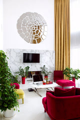 Spiral mirror wall art in a modern workspace with a TV. Marble accent wall, red velvet seating, gold curtains and lush green plants.
