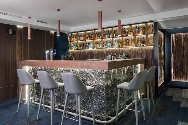 The Vento Silver glass wall panel integrated into a bar counter, featuring a backlit luxury textured glass surface.