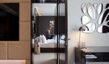 Modern hotel wall decor featuring 11 irregularly shaped chrome mirror drops mounted on a white wall, reflecting the room’s interior.