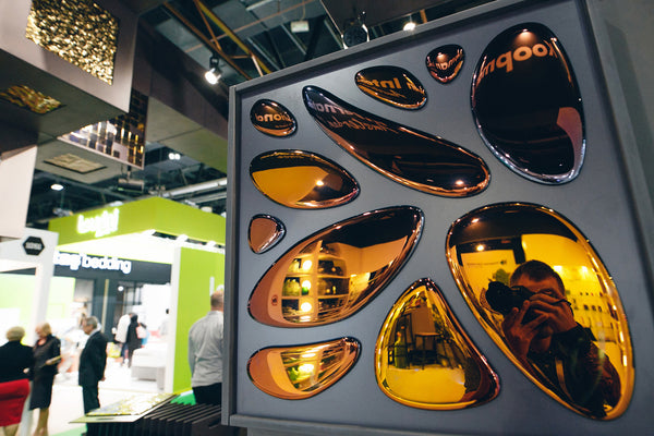 Bronze-tinted mirror wall decor with irregular shapes displayed at an exhibition – reflecting a photographer and surrounding booths