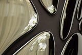 Close-up of modern mirror wall decor with chrome-finished irregular shapes reflecting white orchid flowers and soft curtain folds